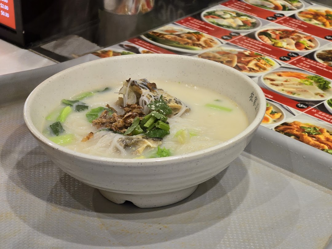 A comforting bowl of milky fish soup with noodles, vegetables, and fried shallots on a tray.