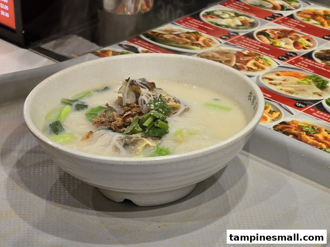 A comforting bowl of milky fish soup with noodles, vegetables, and fried shallots on a tray.