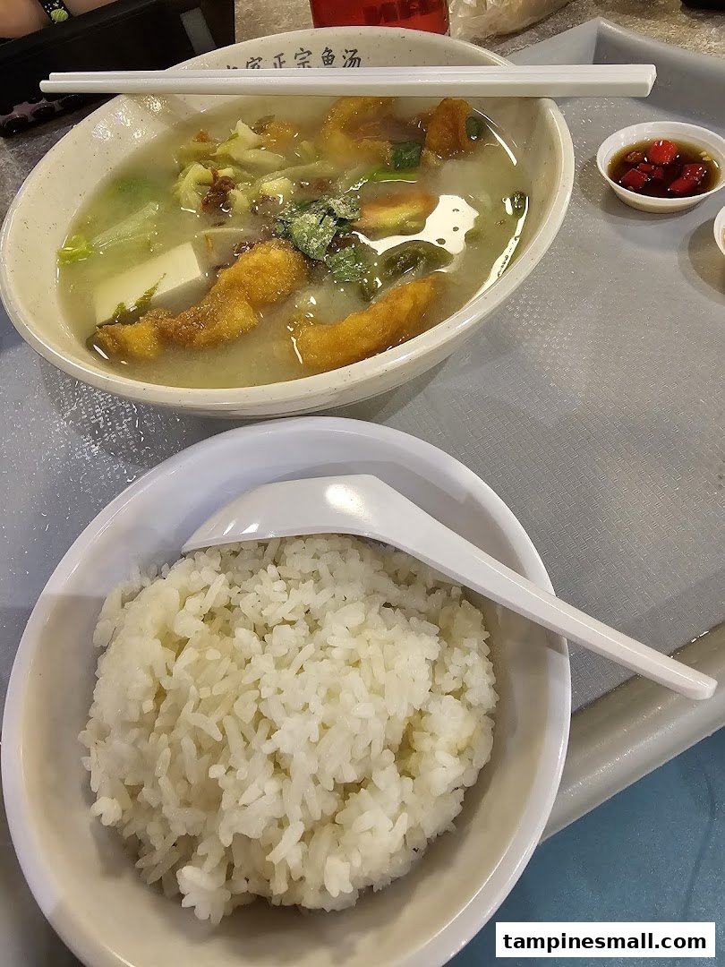 A delicious bowl of fish soup with fried fish, tofu, and vegetables, served with a side of white rice.