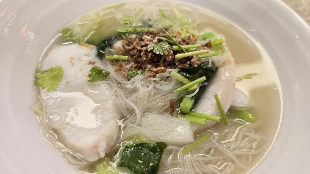 A close-up of a delicious bowl of fish soup with noodles, vegetables, and crispy toppings.