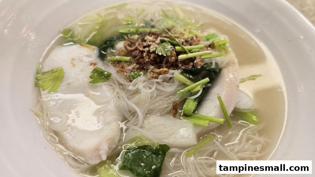 A close-up of a delicious bowl of fish soup with noodles, vegetables, and crispy toppings.