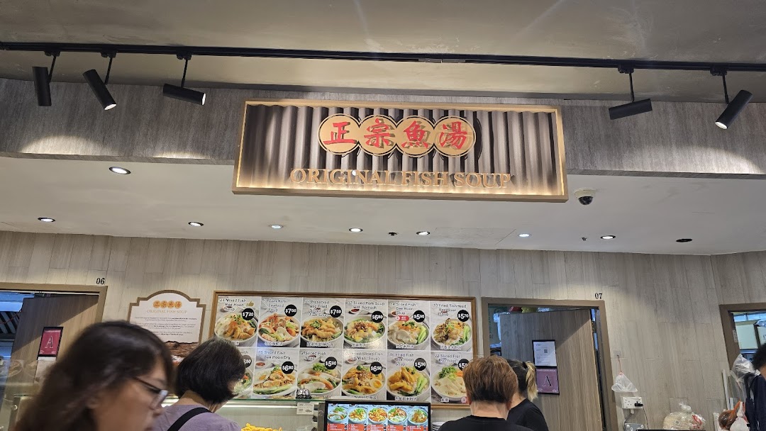 A bustling food stall featuring a large menu board with various fish soup and porridge dishes.