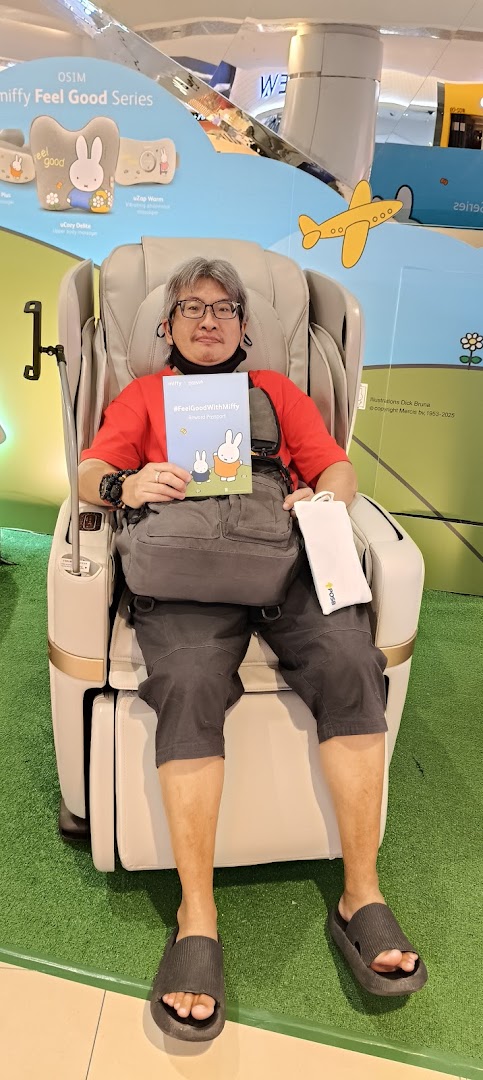 A man relaxes in an OSIM massage chair, holding a Miffy-themed booklet, showcasing wellness products.