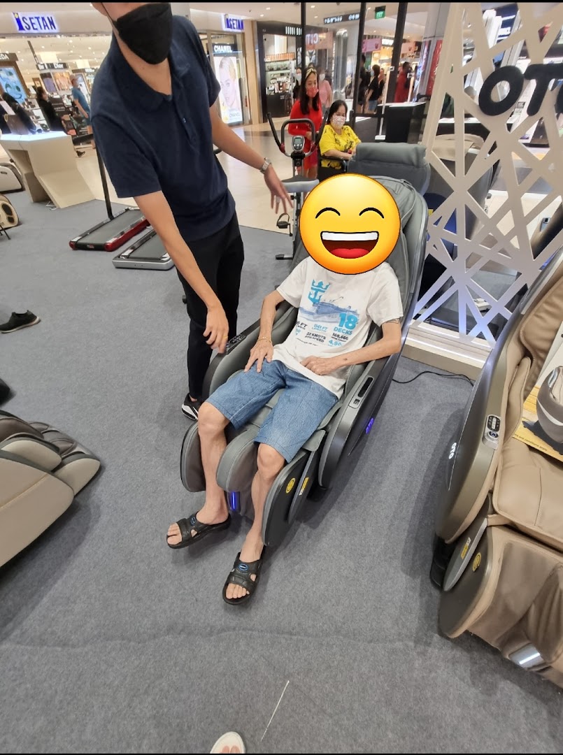 A customer enjoys a massage chair demonstration at OTO Wellness, assisted by a staff member.