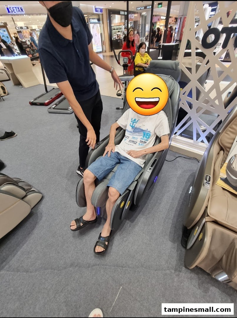 A customer enjoys a massage chair demonstration at OTO Wellness, assisted by a staff member.