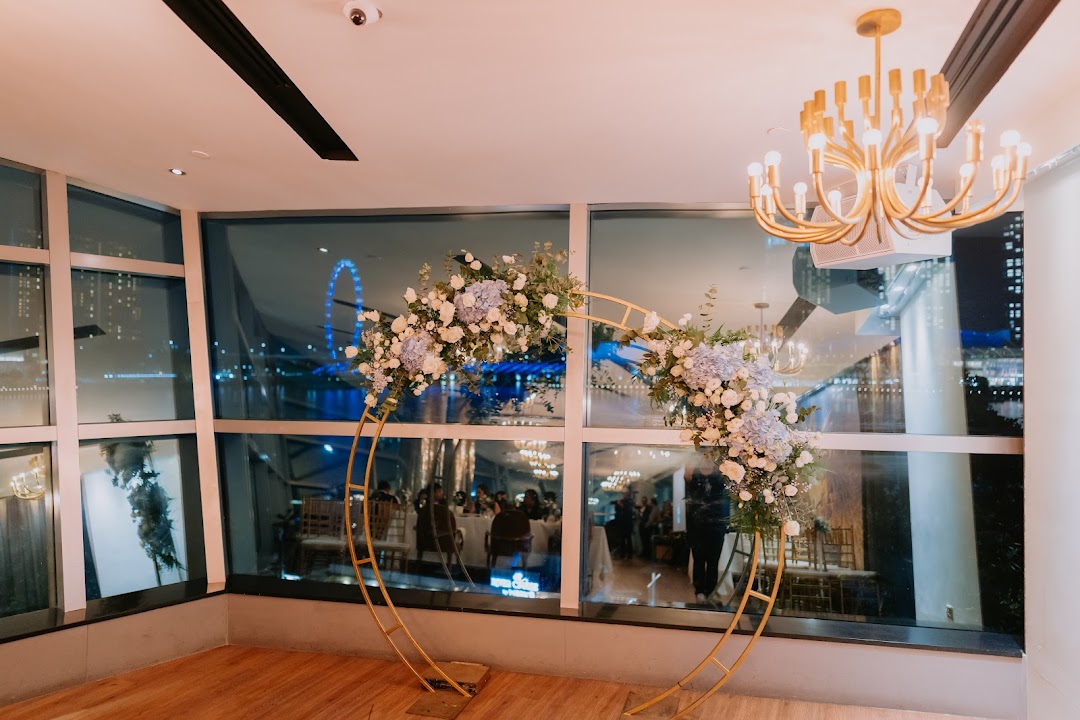 An elegant event space featuring a floral arch, large windows overlooking a city night view, and a golden chandelier.