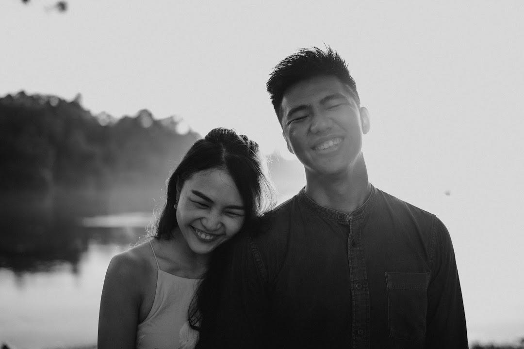 A black and white photo of a happy couple smiling outdoors, likely a pre-wedding or engagement shoot.