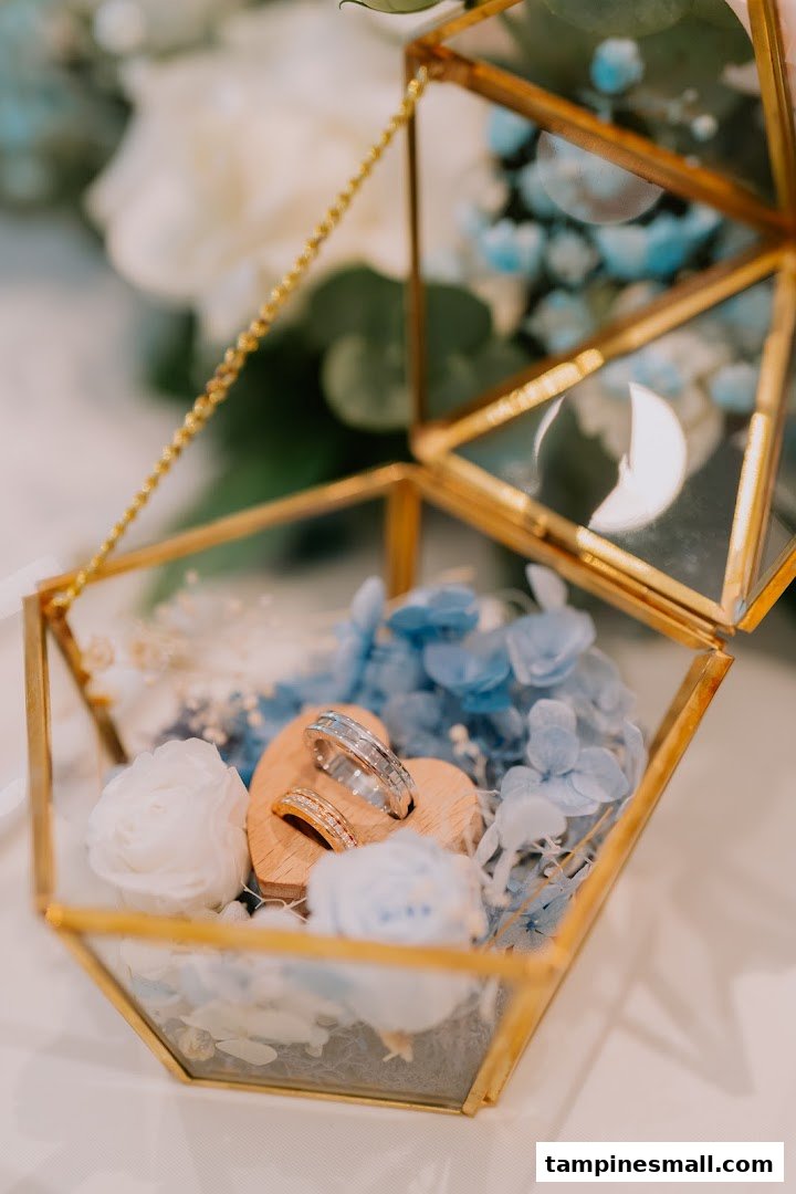 A close-up of two wedding rings displayed in a geometric glass box with blue and white flowers.