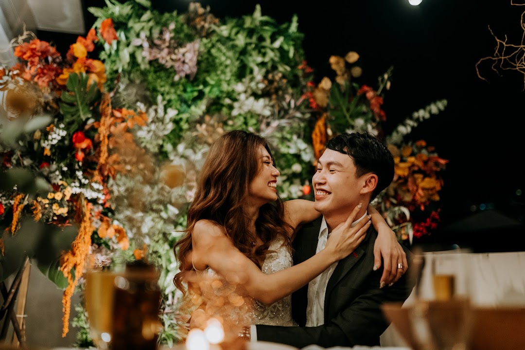 A joyful couple embracing and laughing, surrounded by vibrant floral decorations at an event.