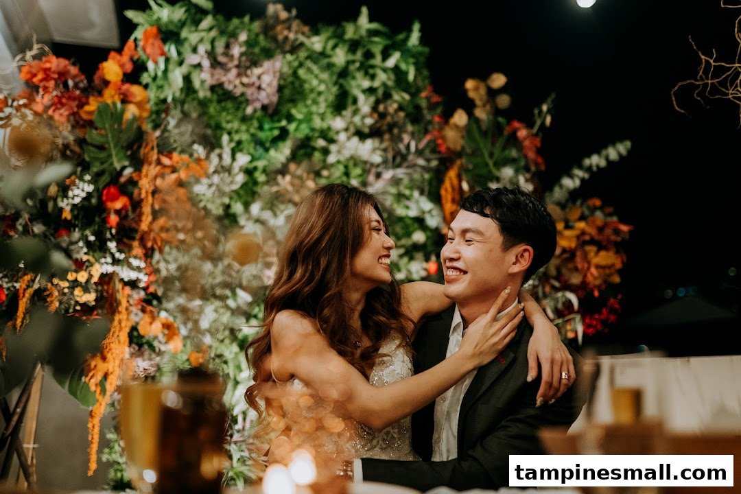 A joyful couple embracing and laughing, surrounded by vibrant floral decorations at an event.