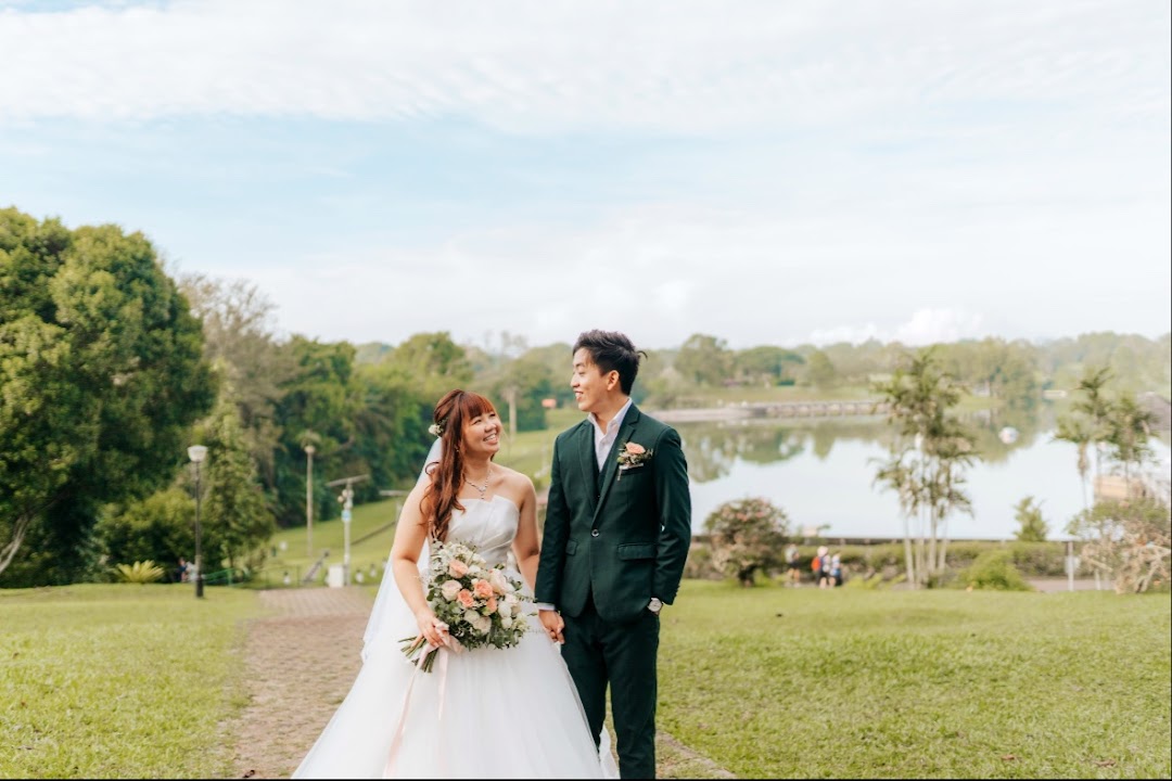 A happy couple in wedding attire holding hands in a scenic outdoor park with a lake.