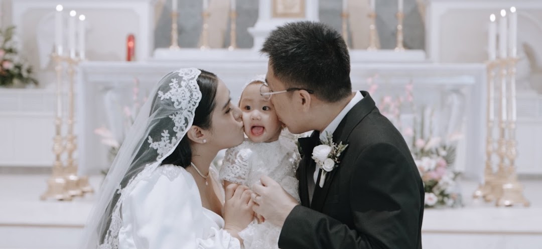 A couple in wedding attire lovingly kisses a baby in a beautiful church setting, capturing a tender family moment.