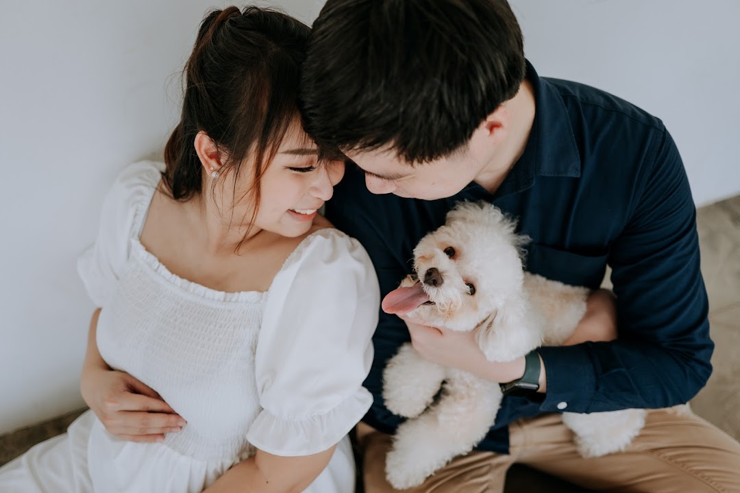 A loving couple embraces their small white dog, capturing a tender, intimate moment.