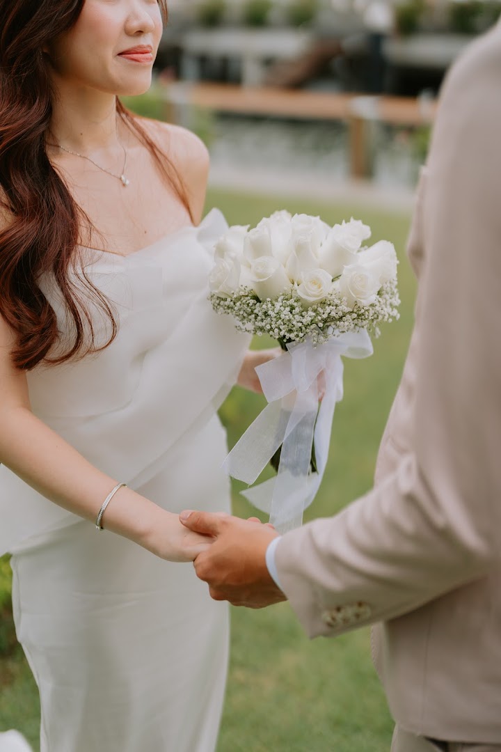 A close-up of a couple holding hands, with the bride holding a beautiful white rose wedding bouquet.