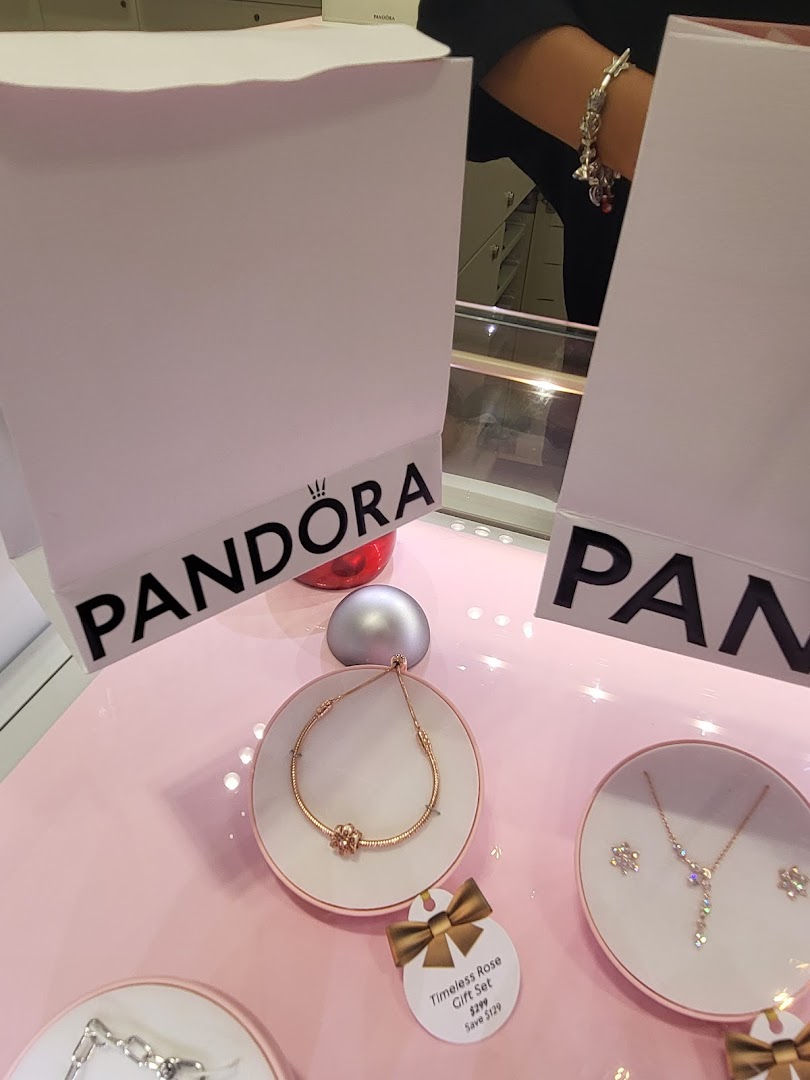 A close-up of Pandora jewelry displays featuring bracelets, necklaces, and gift sets on a pink surface.