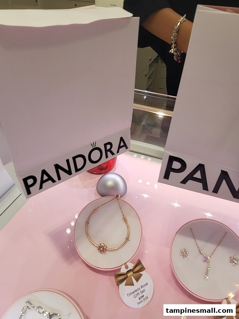 A close-up of Pandora jewelry displays featuring bracelets, necklaces, and gift sets on a pink surface.