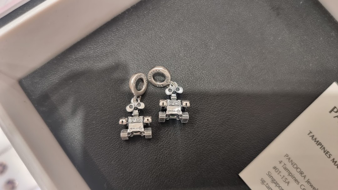 Close-up of two silver Disney WALL-E and EVE charms from Pandora on a black display.