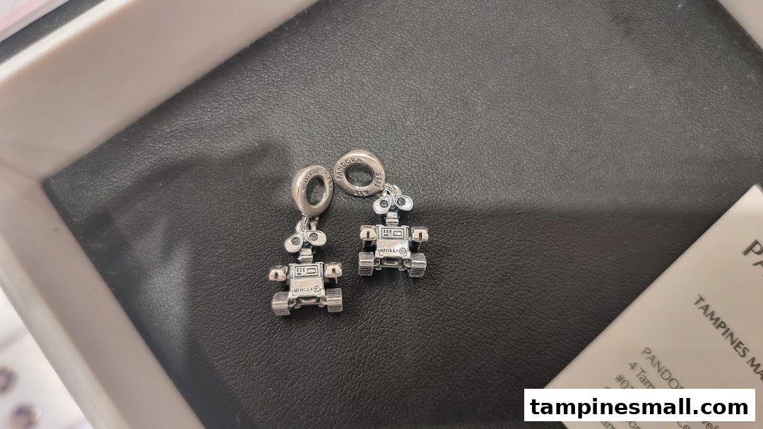 Close-up of two silver Disney WALL-E and EVE charms from Pandora on a black display.