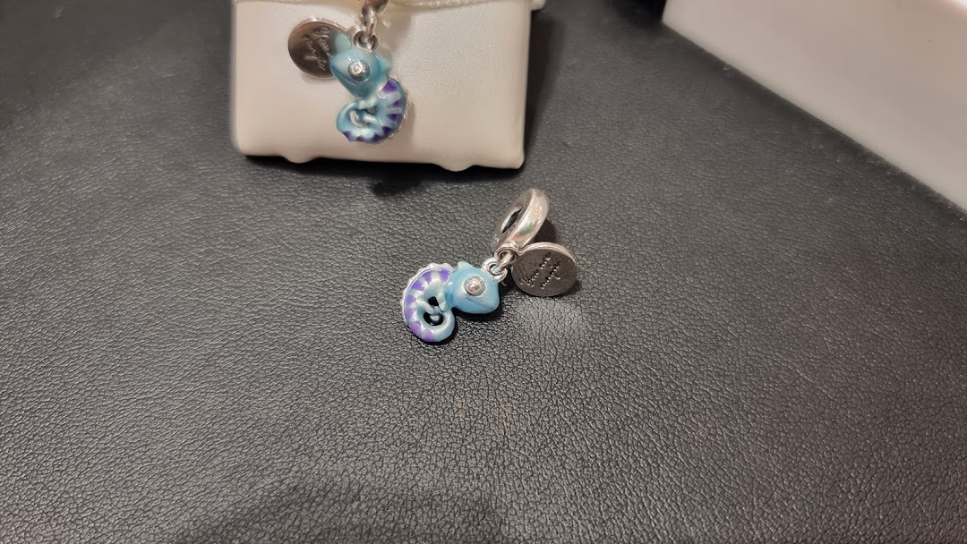 Two colorful chameleon-shaped charms from Pandora, one on a display box and one on a dark surface.