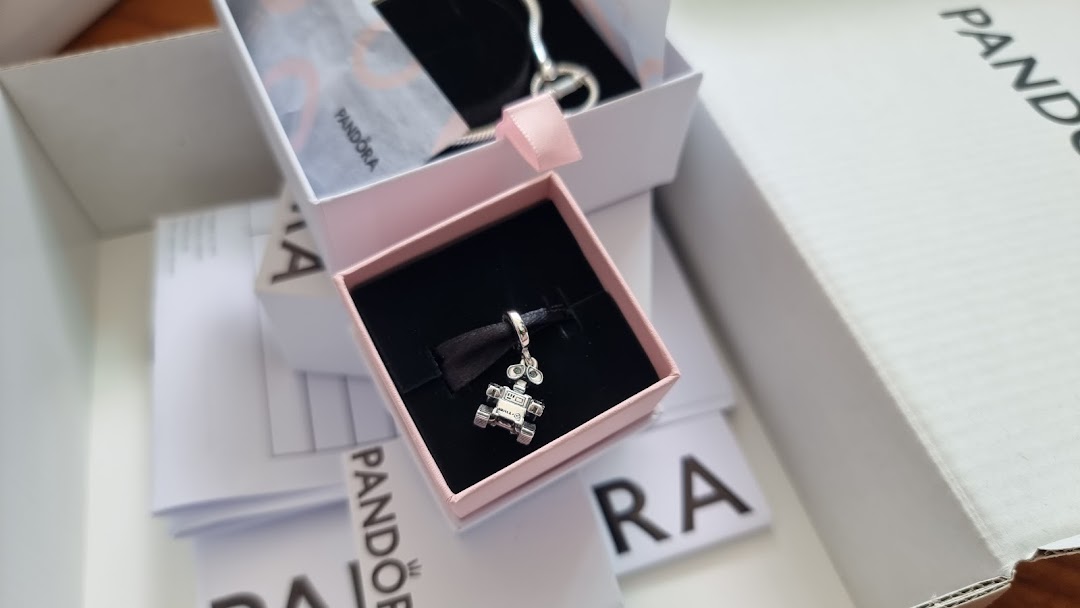 A detailed close-up of a Pandora charm in its signature pink box, surrounded by branded packaging.