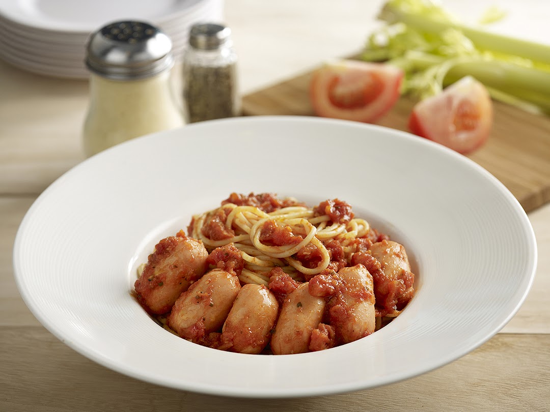 A close-up of spaghetti with sausages and tomato sauce in a white bowl.