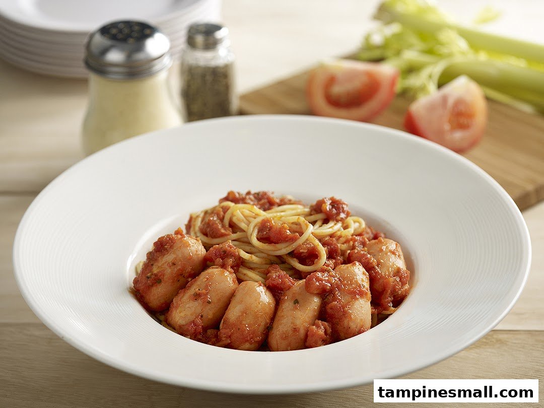A close-up of spaghetti with sausages and tomato sauce in a white bowl.