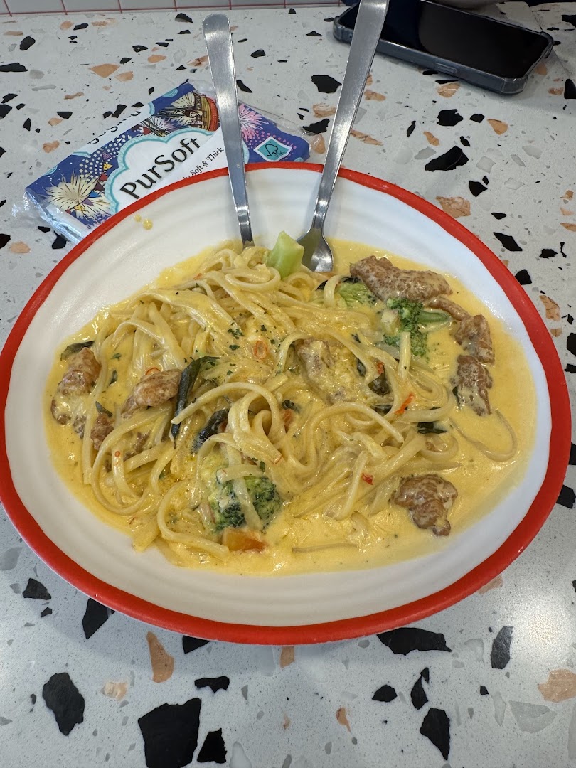 A creamy pasta dish with broccoli and meat, served on a white plate with red rim.