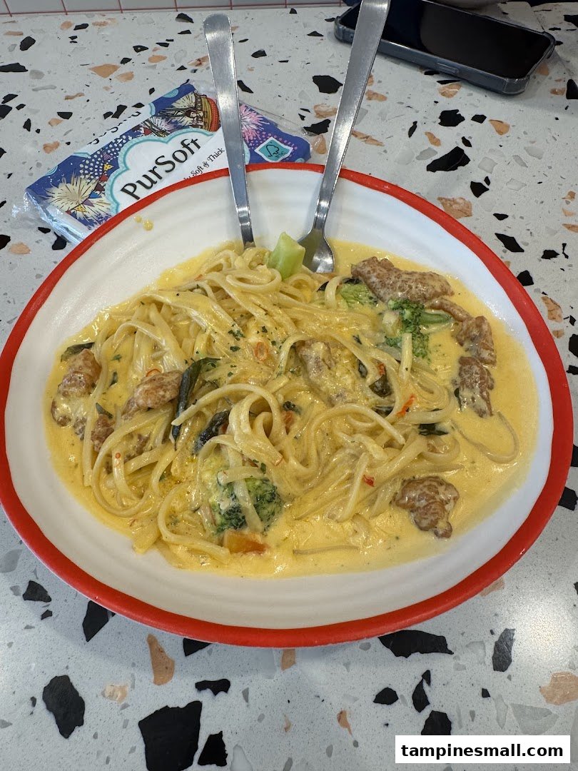 A creamy pasta dish with broccoli and meat, served on a white plate with red rim.