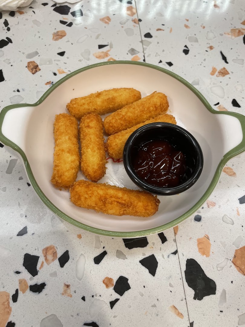 A plate of golden-brown fried mozzarella sticks with a side of dipping sauce on a speckled table.