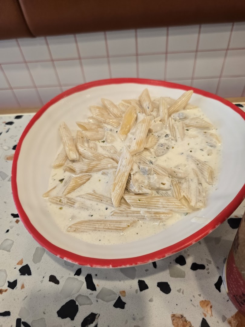 A close-up of penne pasta in a creamy white sauce, served in a white bowl with a red rim.