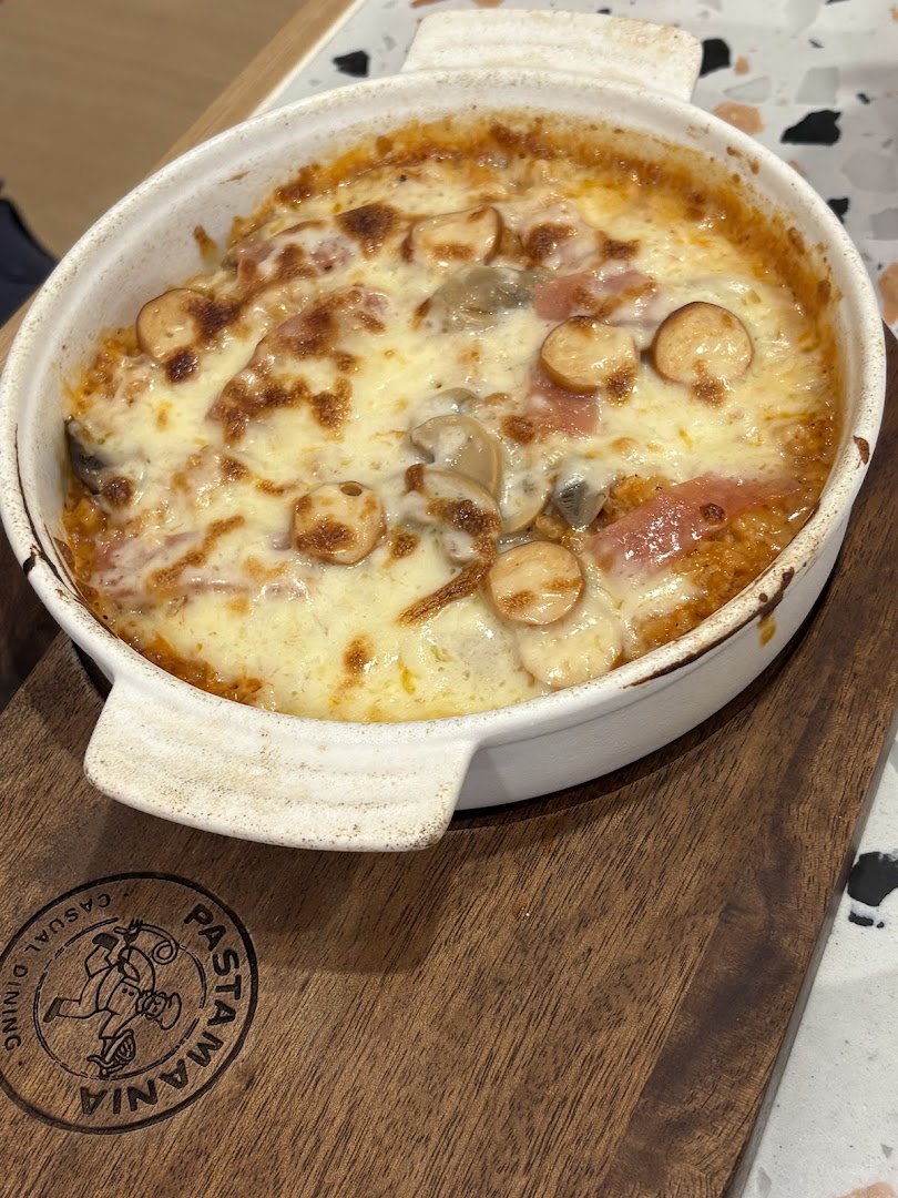 A bubbling baked pasta dish with melted cheese, mushrooms, and sliced sausages in a white ceramic dish.