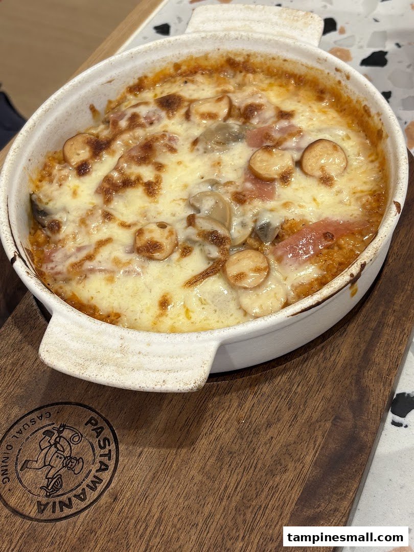 A bubbling baked pasta dish with melted cheese, mushrooms, and sliced sausages in a white ceramic dish.