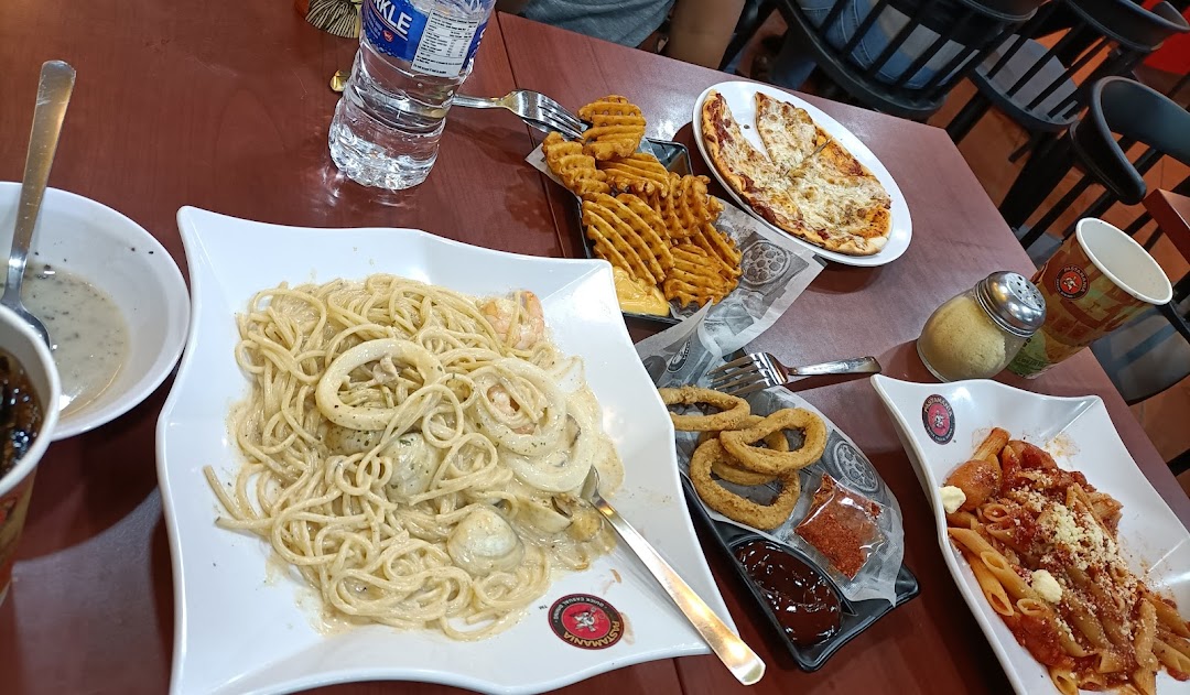 A table filled with various Italian dishes including pasta, pizza, waffle fries, and onion rings.