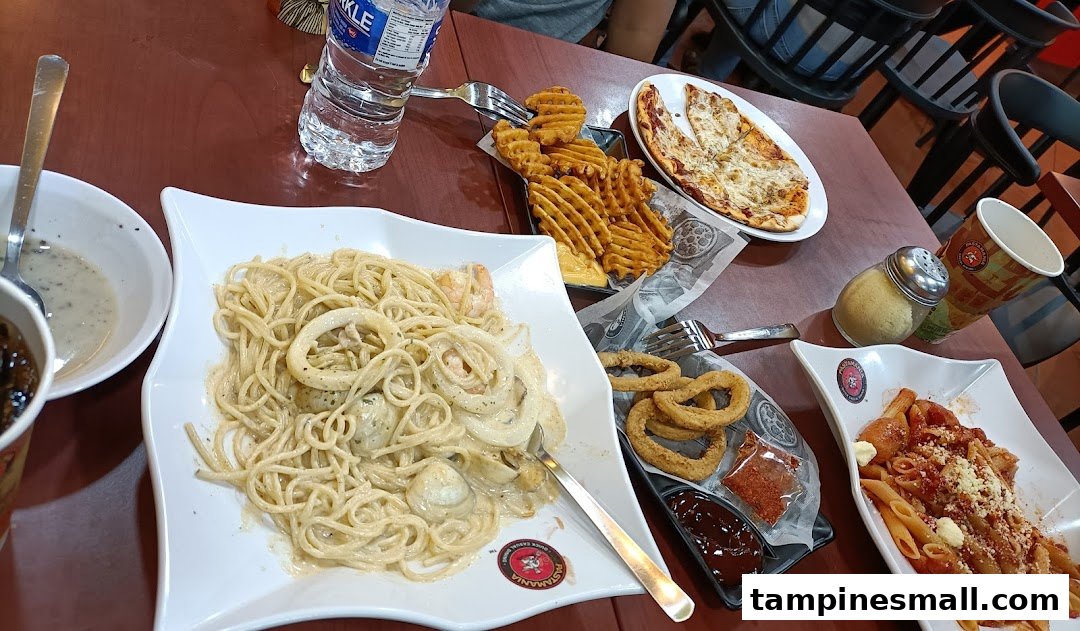 A table filled with various Italian dishes including pasta, pizza, waffle fries, and onion rings.