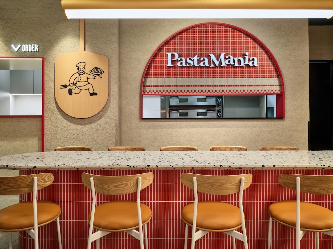 A modern interior view of PastaMania featuring a counter, seating, and the brand's logo.