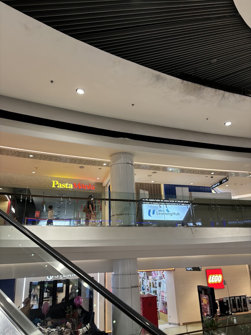 The PastaMania shopfront is visible on an upper level of a bustling shopping mall, viewed from an escalator.