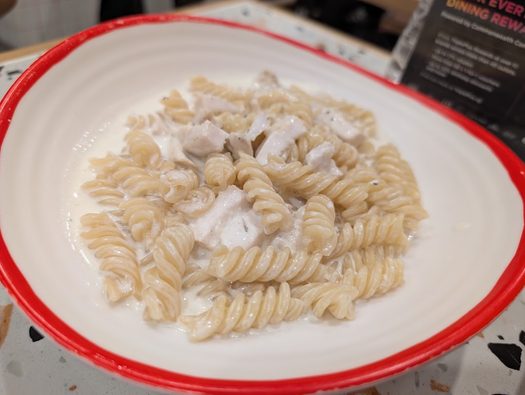 A close-up of fusilli pasta with creamy white sauce and chicken pieces in a white bowl.