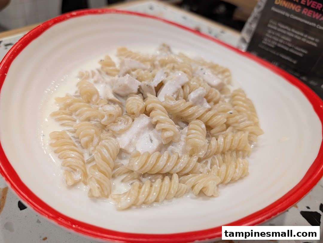 A close-up of fusilli pasta with creamy white sauce and chicken pieces in a white bowl.