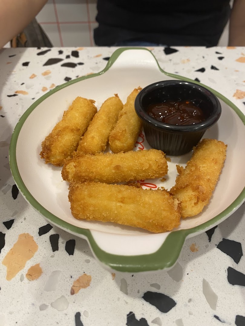 A plate of golden-fried mozzarella sticks with a side of dipping sauce on a speckled table.