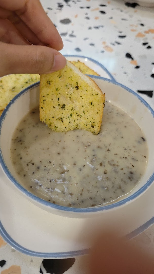 A hand dips a piece of garlic bread into a creamy bowl of mushroom soup.