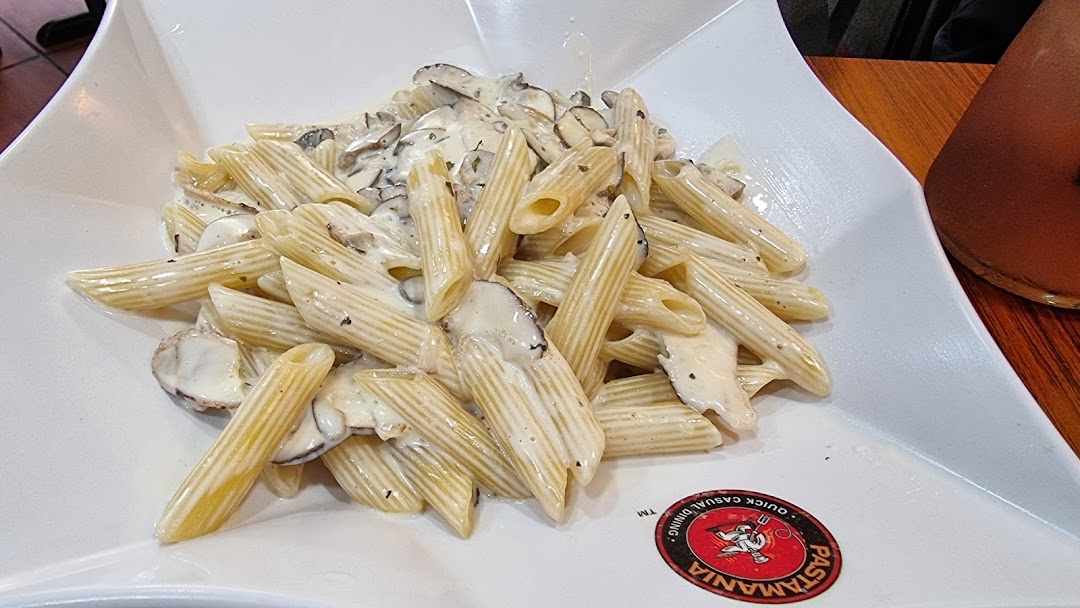 A close-up of creamy penne pasta with mushrooms served in a white dish at PastaMania.