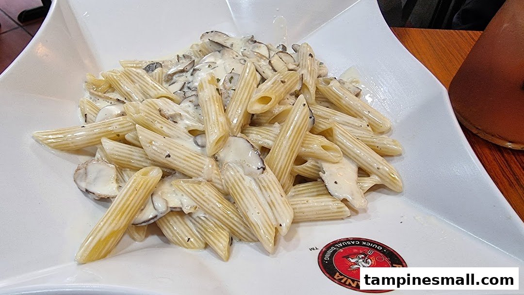A close-up of creamy penne pasta with mushrooms served in a white dish at PastaMania.