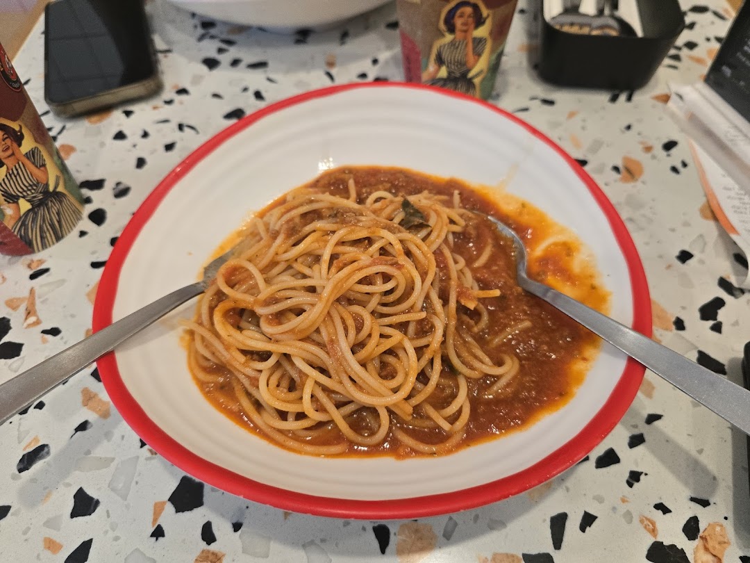 A close-up of a plate of spaghetti with rich tomato sauce on a patterned table.