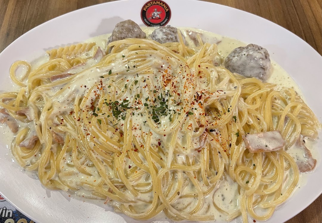 A creamy pasta dish with spaghetti, meatballs, and bacon, garnished with herbs and chili flakes.