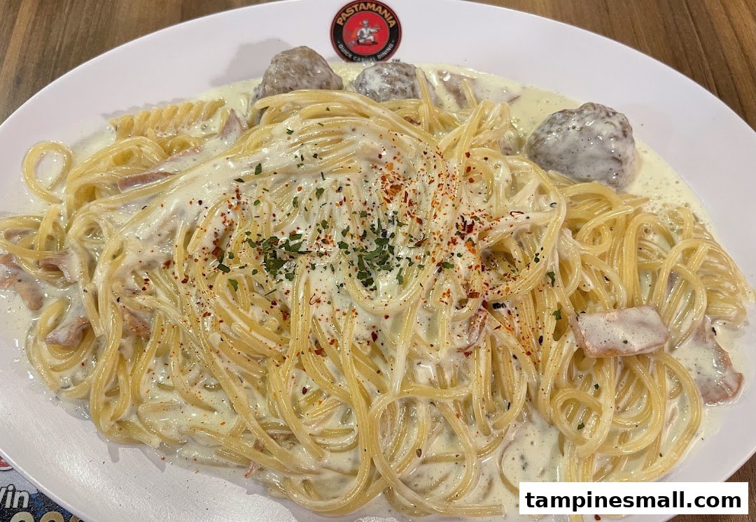 A creamy pasta dish with spaghetti, meatballs, and bacon, garnished with herbs and chili flakes.