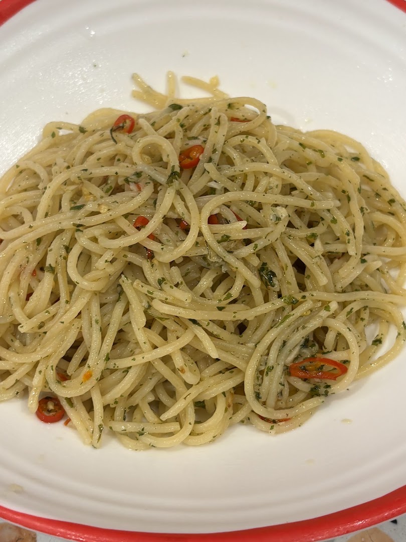 A close-up of spaghetti aglio e olio with chili and herbs in a white bowl.
