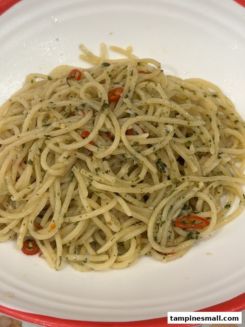 A close-up of spaghetti aglio e olio with chili and herbs in a white bowl.
