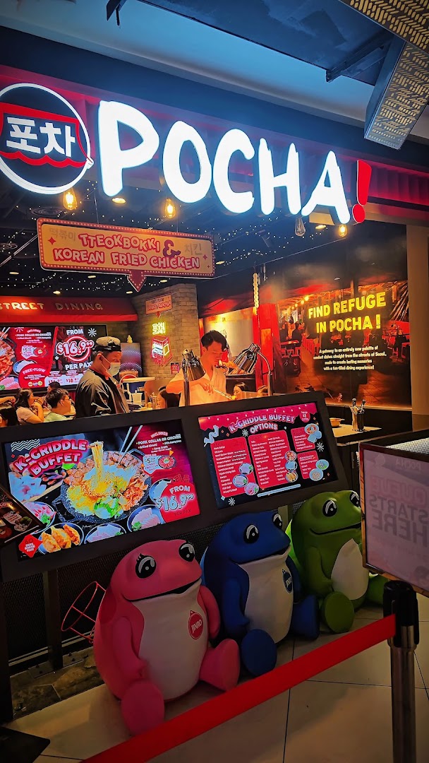 Brightly lit entrance of POCHA! Korean Street Dining, featuring signage, menu displays, and colorful frog mascots.