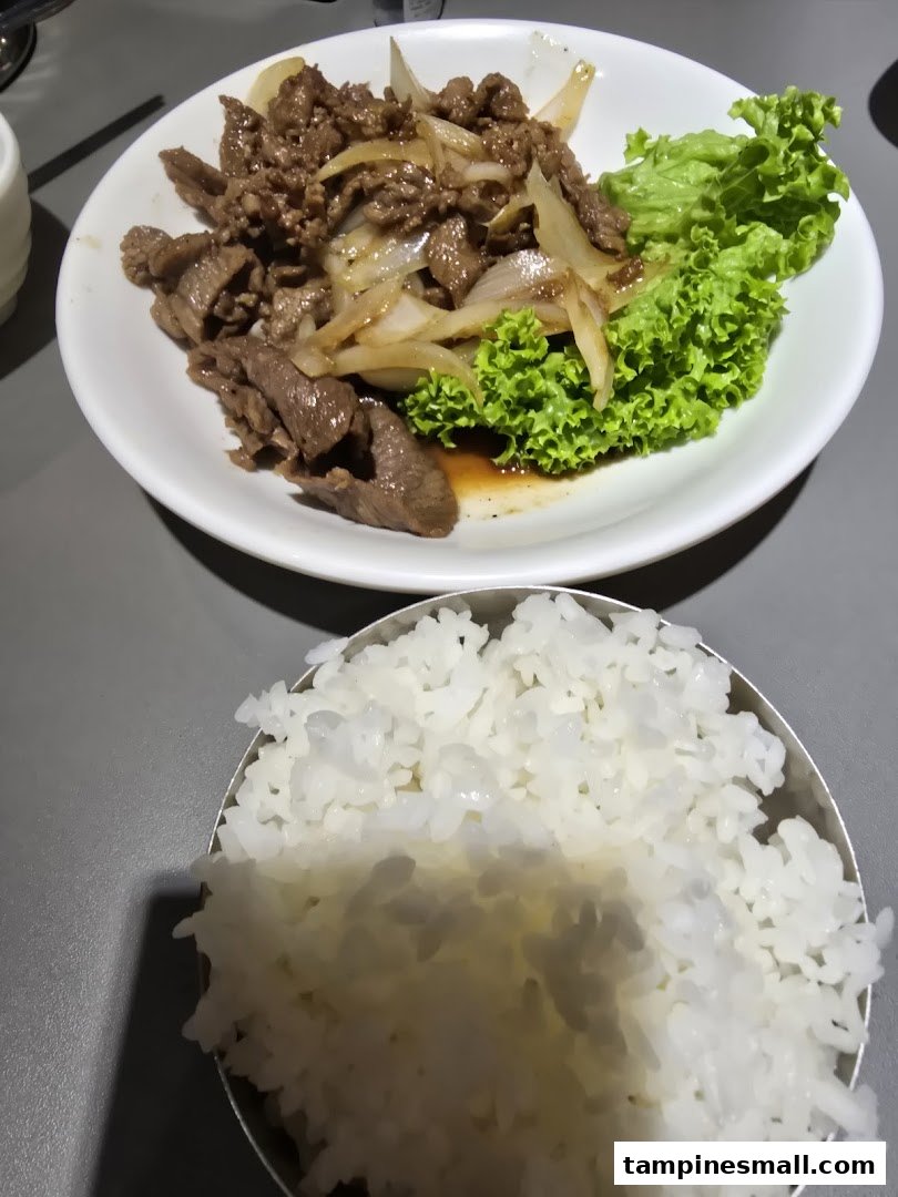 A delicious plate of Korean bulgogi-style beef with onions and fresh lettuce, served with a bowl of white rice.