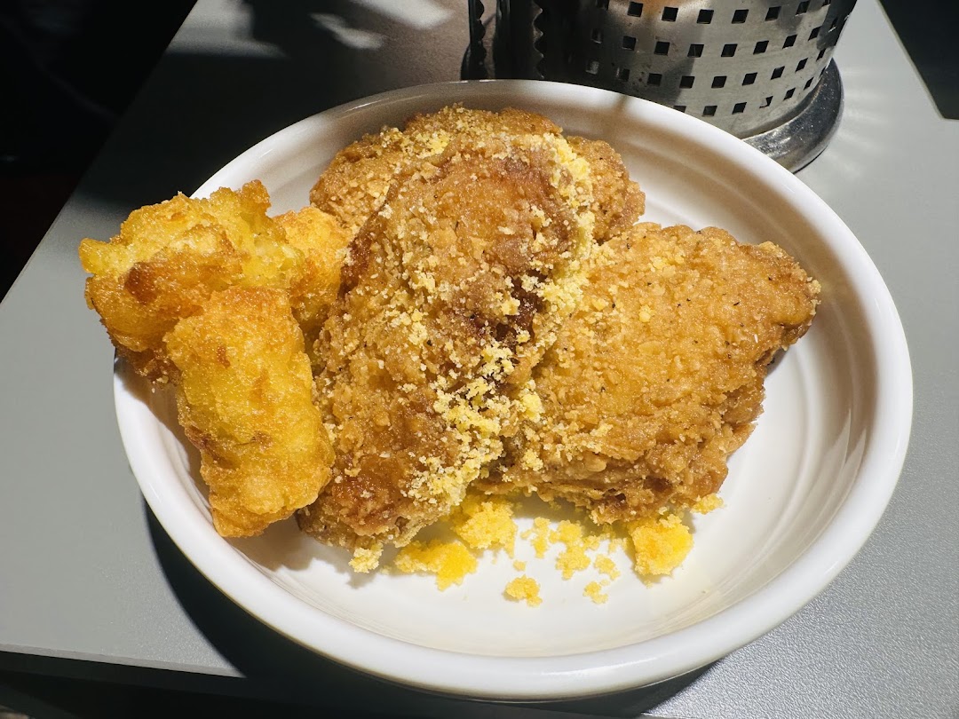 A white bowl filled with crispy fried chicken pieces and golden potato tots, sprinkled with yellow powder.